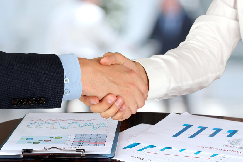 Dos profesionales de negocios estrechándose la
mano sobre una mesa con documentos, simbolizando un
acuerdo o colaboración.