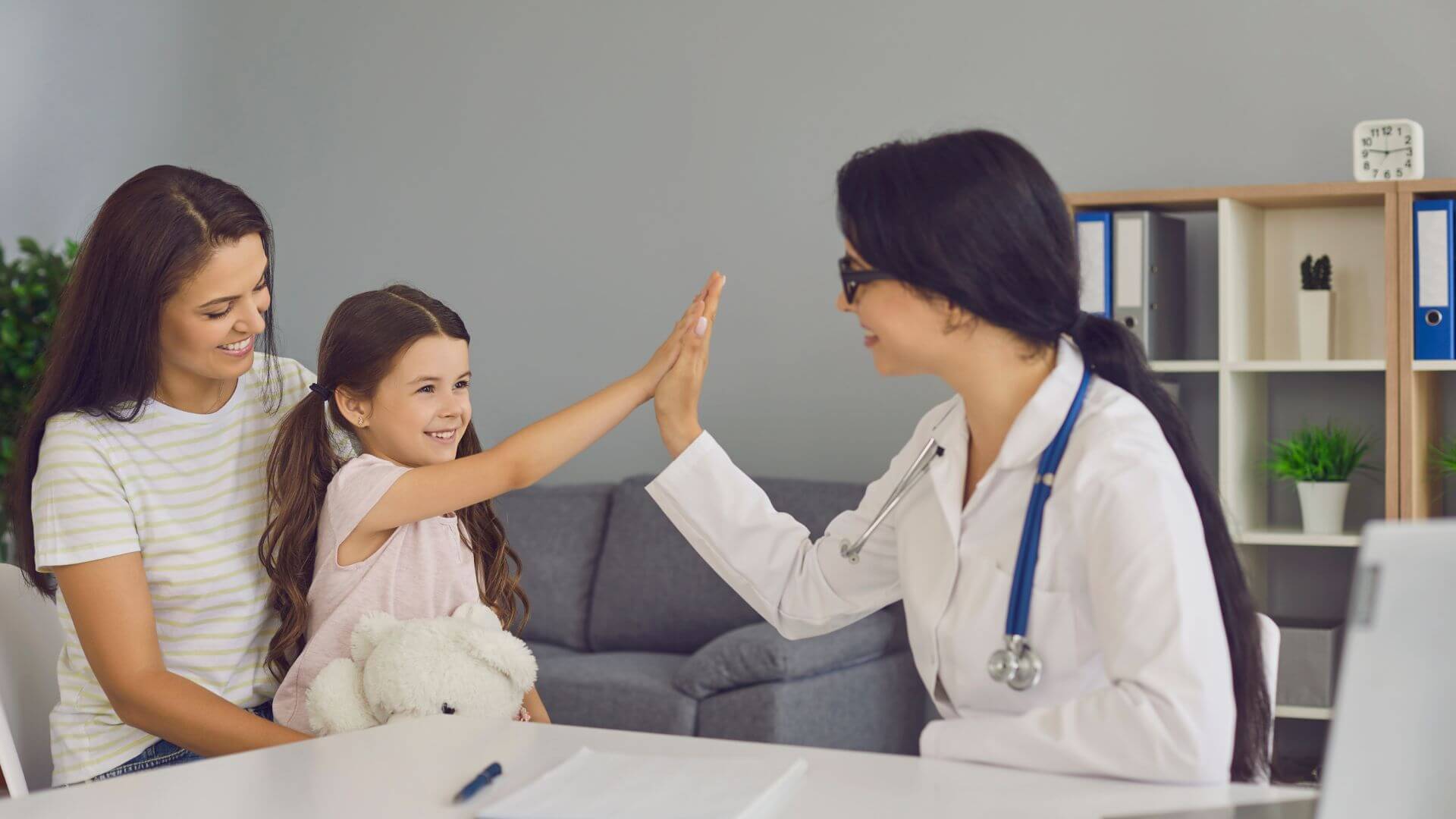 Una mujer y un niño sentados en un escritorio
mientras un médico les da un saludo con la mano.